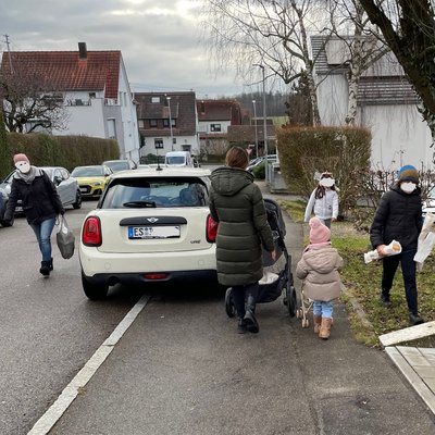 Zu-Fuß-Gehende quetschen sich auf dem restlichen Gehweg, im Vorgarten eines Hauses und auf der Fahrbahn an einem auf dem Gehweg geparkten Auto vorbei.