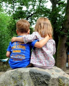 Zwei Kinder sitzen Arm in Arm auf einem Stein